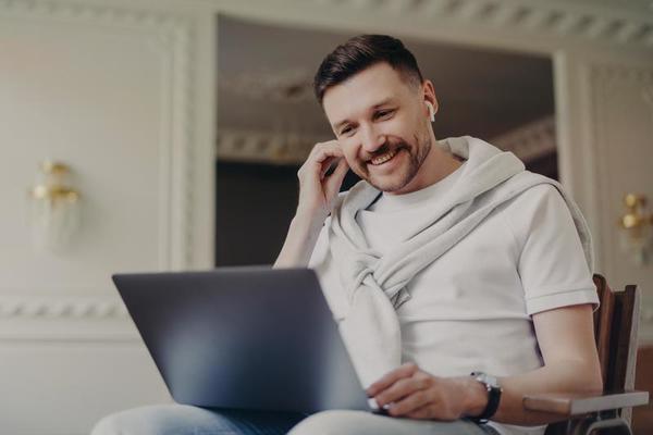 cheerful-man-freelancer-adjusting-earpiece-and-looking-at-laptop-while-talking-by-video-chat-with-colleagues-photo